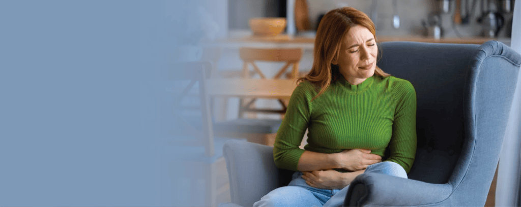 Women sitting in a chair in a house, clutching her abdomen with a pained look on her face